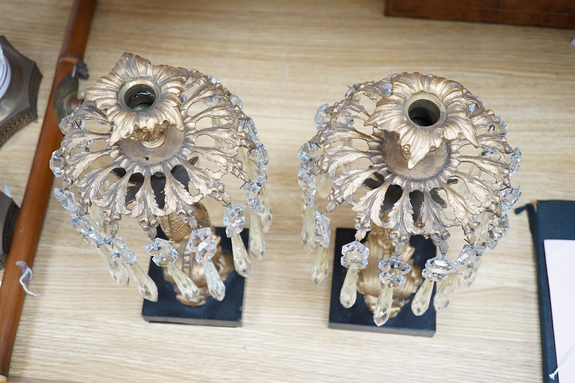 A pair of William IV gilt metal candlesticks, the stems formed as dolphins, with glass lustre drops, raised on square slate bases, 37cm high